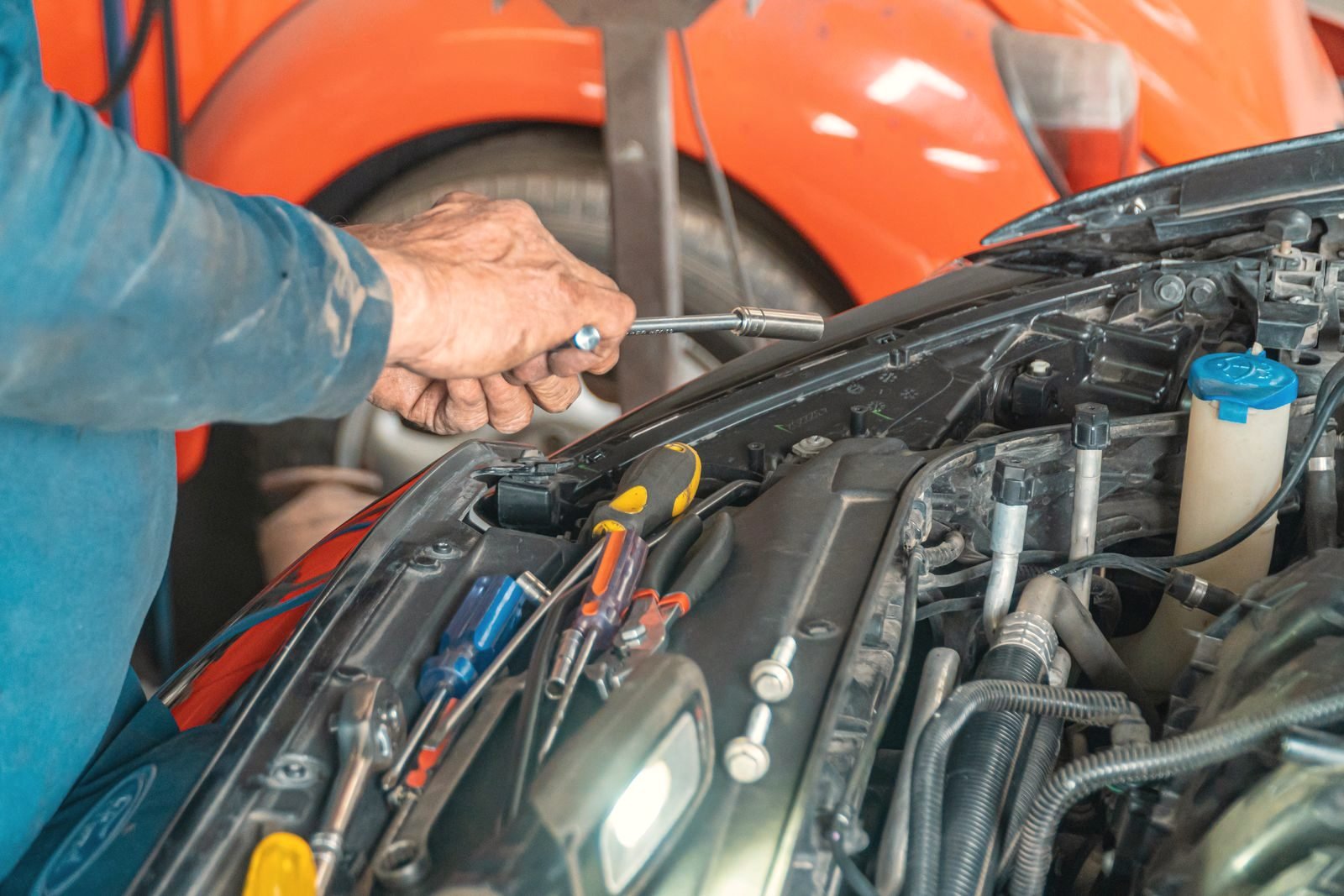 Hands working inside the engine bay of a car with the hood open