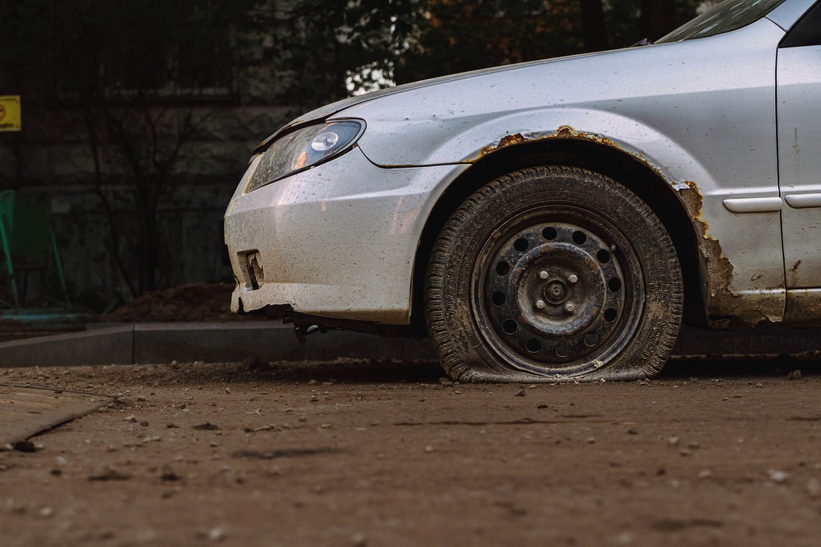 A car with a flat front tire stopped on the gravel shoulder