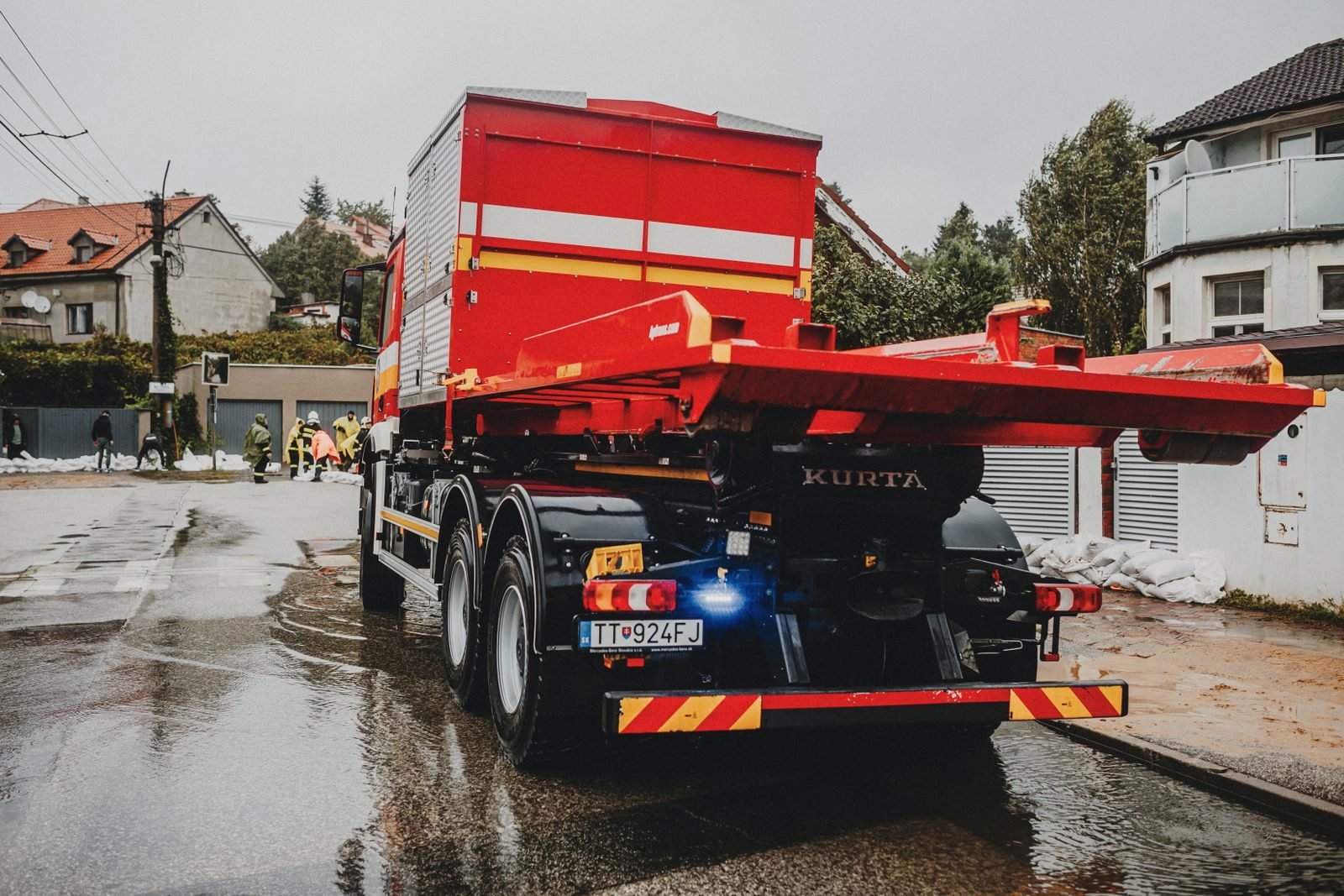 A red tow truck with its carrier bed lowered on a wet residential street