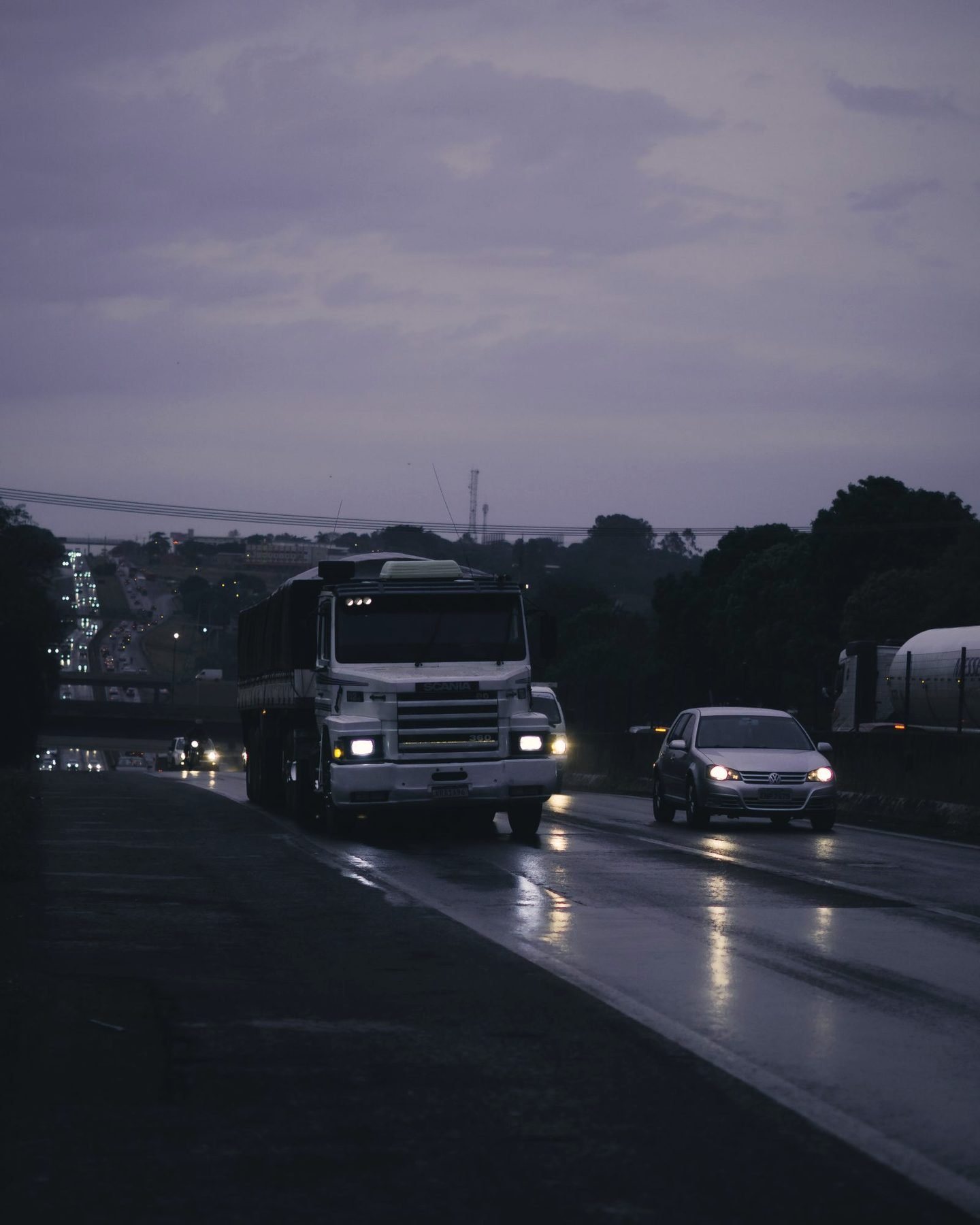 A wet highway at twilight with trucks under a grey sky